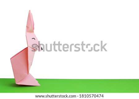 Pink origami rabbit on white (isolated) and green background. Easter bunny on the grass. Minimalistic illustration. Paper craft. Background with place for your design