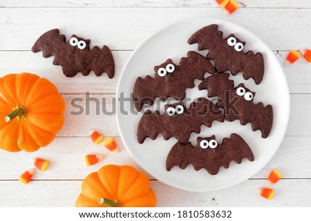 Halloween bat cookies, above view with pumpkins on a white wood background