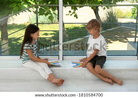 Little children with rainbow paintings near window indoors. Stay at home concept