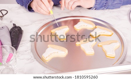 Decorating ice skate shaped sugar cookies with white color royal icing.