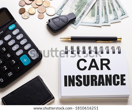 CAR INSURANCE is written in a white notepad near the car key, cash, calculator and pen. Insurance concept