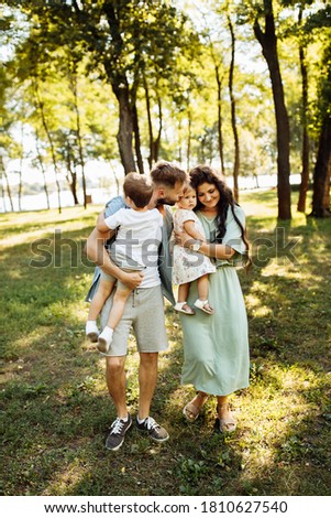 Beautiful family with little kids at the park, loving parents hold adorable children in arms, smiling, caring father kiss little daughter, enjoy happy moments, parenting concept