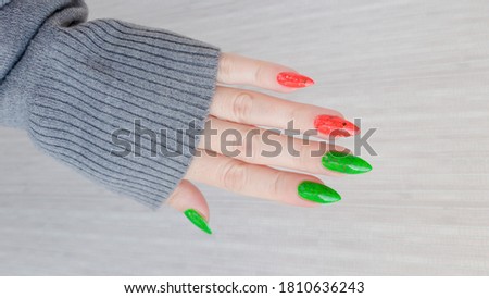 Woman's hand with long nails and green manicure with bottles of nail polish