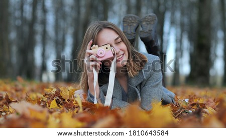 A young beautiful girl takes pictures in an autumn park using a toy camera.
