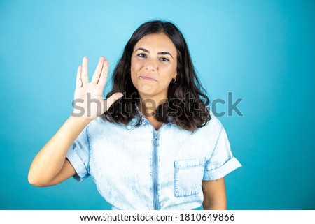 Young beautiful woman wearing a denim jumpsuit over isolated blue background doing hand symbol.