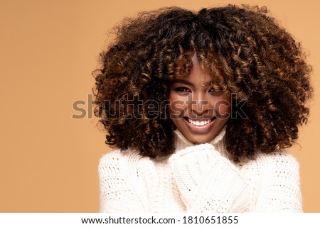 Happy beautiful african girl with afro hairstyle posing in cozy sweater on beige studio background. Royalty-Free Stock Photo #1810651855