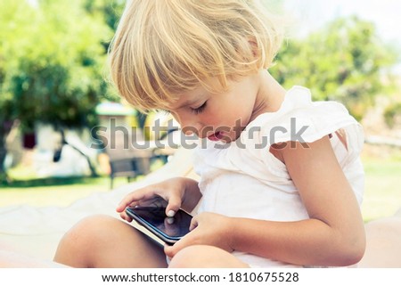 Little girl playing game or watching something on mobile smart phone.