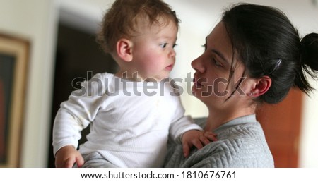 Casual mother holding and loving baby. Mom kissing infant boy at home indoors. Real life love and cuddle