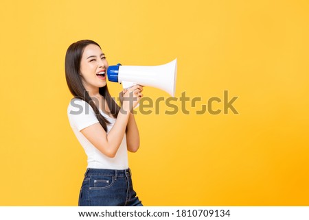 Happy beautiful Asian woman talking on magaphone isolated on yellow background with copy space Royalty-Free Stock Photo #1810709134