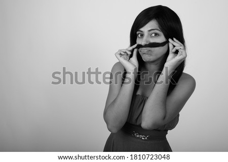 Studio shot of young Persian woman using hair as mustache while wearing dress against gray background