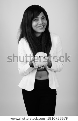 Portrait of happy young Persian businesswoman holding piggy bank