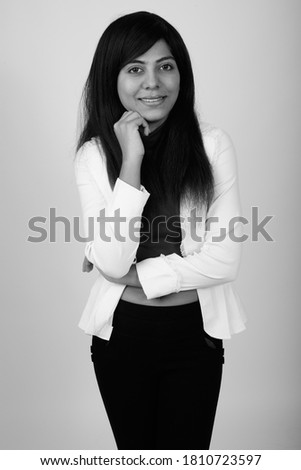 Studio shot of young happy Persian businesswoman smiling while thinking against gray background
