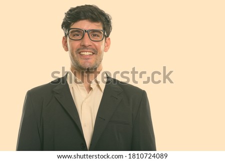 Studio shot of young happy Persian businessman smiling while wearing eyeglasses