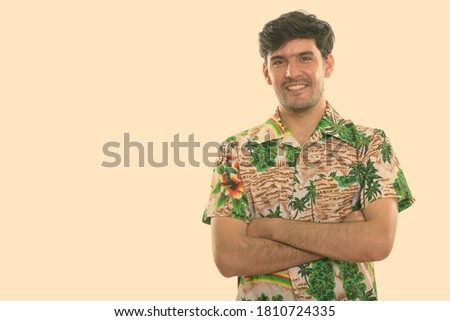 Studio shot of young happy Persian man smiling with arms crossed