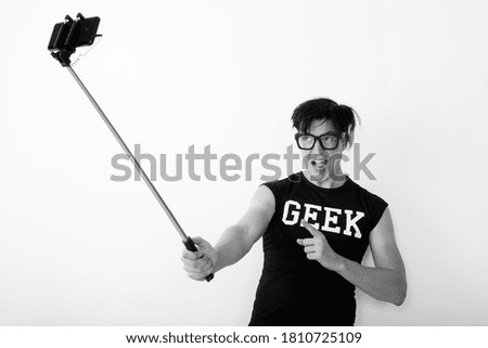 Happy young handsome nerd man pointing finger and taking selfie with phone on selfie stick