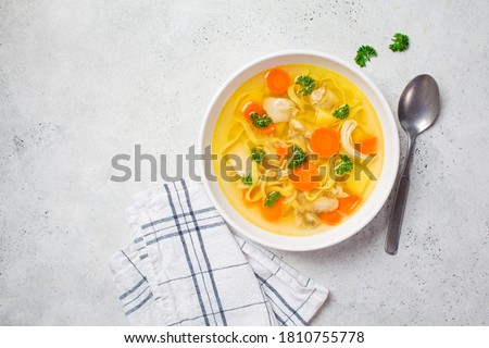 Homemade chicken soup with noodles and vegetables in a white bowl, white background. Healthy warm comfortable food. Royalty-Free Stock Photo #1810755778