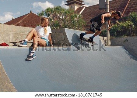 Skater Friends In Skatepark. Girl Sitting On Concrete Ramp, Guy Riding On Skateboard. Casual Outfit For Summer Skateboarding. Extreme Sport As Lifestyle Of Urban People.