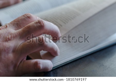 Mature male hand from above on an open book. Thick hardcover book. Male hand with a book on a black table. Selective focus.