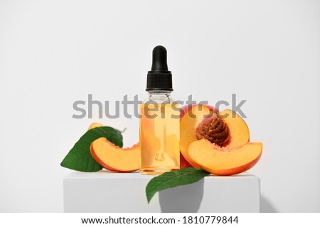 Fragrant peach essential oil on a white stand. An aromatic fruit spa oil for skin care. Alternative homeopathic medicine product in a transparent bottle with a pipette. Royalty-Free Stock Photo #1810779844