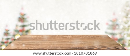 Perspective wood table with blur Christmas tree decorate string light and blue bokeh with snow light.Panoramic wooden countertop banner mock up for product display greeting card design online content
