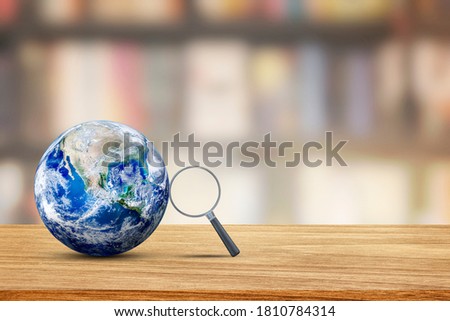 Learning and Education Concept : Magnifying glass lean on blue planet earth with blurry image of library room in background. (Elements of this image furnished by NASA.)