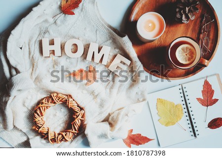 cozy autumn table, top view of still life details in hygge style on white background. Tea with lemon, woolen sweater, dried leaves and notepad.