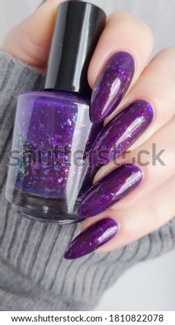 Female hand with long nails and purple lilac manicure holds a bottle of nail polish