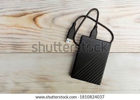 External compact SSD-drive with USB cable on wood background