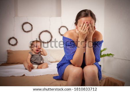 Mom is tired of the baby, wants to rest and sleep. The child screams, hysterical. The woman is tired of the child's cry, she does not want to hear. A one-year-old girl yells from a toothache. Royalty-Free Stock Photo #1810833712