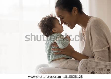Smiling young african american affectionate mommy holding on laps little cute toddler baby, touching noses, copy space for care devotion text. Loving mixed race mother spending time with adorable kid. Royalty-Free Stock Photo #1810838128