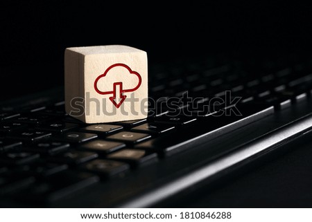 Cloud computing download icon on wooden cube with computer keyboard against black background. Remote download technology concept.