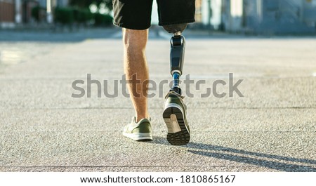 Low angle view at disabled young man with prosthetic leg walking along the street Royalty-Free Stock Photo #1810865167