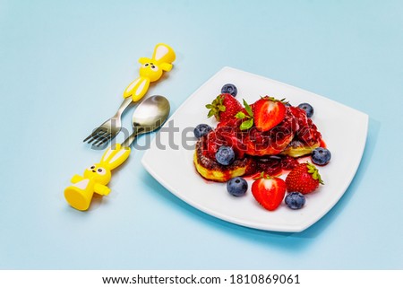 Cottage cheese pancakes with fresh berries and strawberry sauce. Healthy and funny breakfast concept for kids. Ripe blueberry, fragrant mint leaves, cutlery. Gentle blue background, copy space