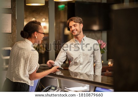 A female hotel receptionist taking the contactless payment of a customer who is checking in to the hotel, he is using his smart phone to pay. Royalty-Free Stock Photo #1810879660