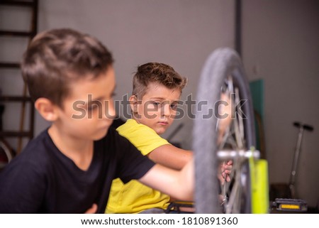 Two boys are sitting in the garage repairing their bike