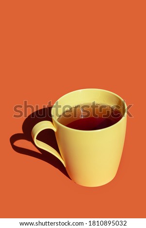hot tea in a yellow plastic cup against orange background. hard light and deep shadows picture with space for text 
