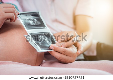 Happiness pregnant woman is holding her stomach and a photo of her Ultrasound with her husband at living room in the morning
