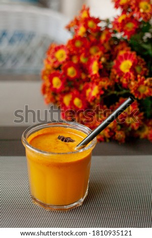 Autumn drink in glass with tube and piece of star anise on the background of bouquet of bright orange asters on the outdoor terrace. Sea buckthorn smoothie