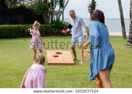Family playing cornhole game by the sea on sunny summer day. Parents and children playing bean bag toss Royalty-Free Stock Photo #1810937524