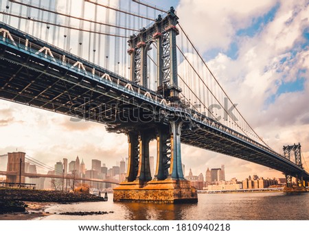 Manhattan Bridge over East River at sunset in New York City, USA. Beautiful skyline with skyscrapers. Panoramic view from Brooklyn waterfront. Urban perspective.