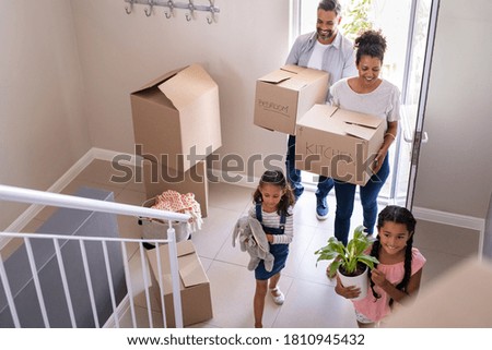 Ethnic family with two children carrying boxes and plant in new home on moving day. High angle view of happy smiling daughters helping mother and father with cardboard boxes in new house. Royalty-Free Stock Photo #1810945432