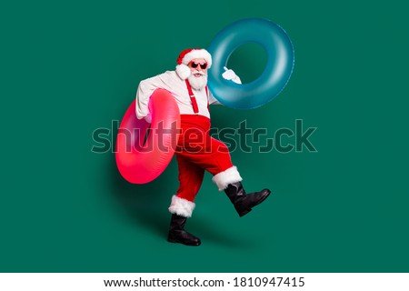 Full length body size view of his he nice handsome bearded funny cheerful cheery overweight fat Santa holding in hands carrying rubber rings having fun poolside resort isolated green color background