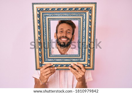 Handsome caucasian man with beard holding empty frame celebrating crazy and amazed for success with open eyes screaming excited. 