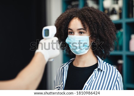 Young black woman in protective mask getting temperature check up in salon, close up