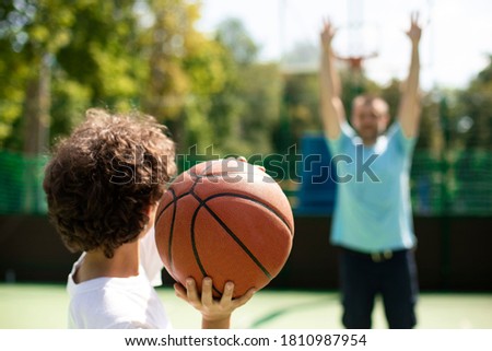 Back view of small basketball player throwing ball to man in blurred background