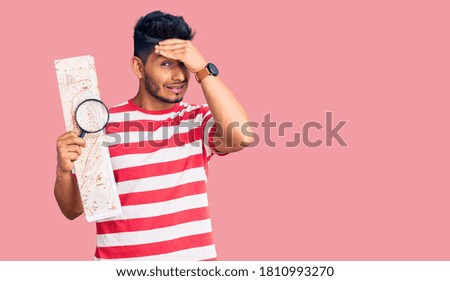 Handsome latin american young man looking at city map with magnifying glass stressed and frustrated with hand on head, surprised and angry face 