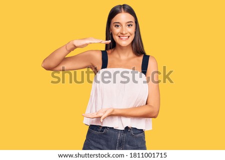 Young hispanic woman wearing casual clothes gesturing with hands showing big and large size sign, measure symbol. smiling looking at the camera. measuring concept. 