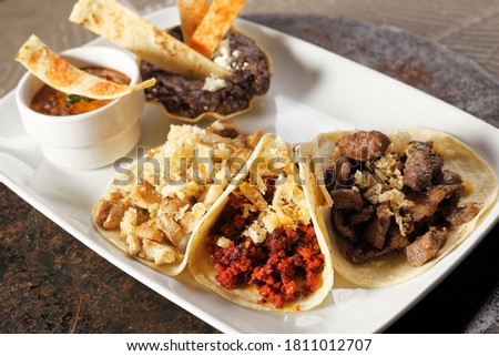 Roast beef tacos, roasted chicken and chorizo with pork rinds accompanied with refried beans and spicy sauce.