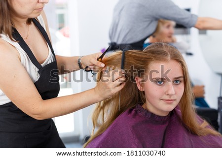 Closeup of long-haired teen girl getting haircutting by professional hairdresser in salon..