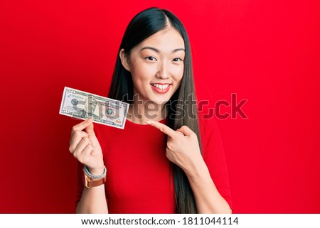 Young chinese woman holding 50 dollars banknote smiling happy pointing with hand and finger 